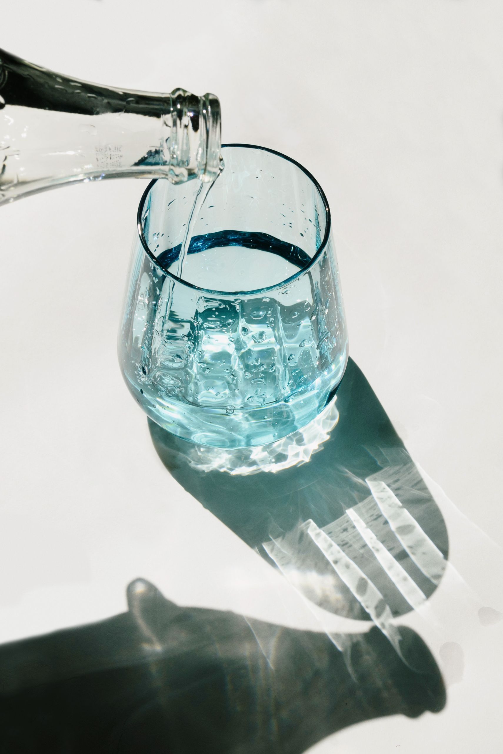 Closeup of water being poured into a glass, with artistic shadow play on a sunny day.