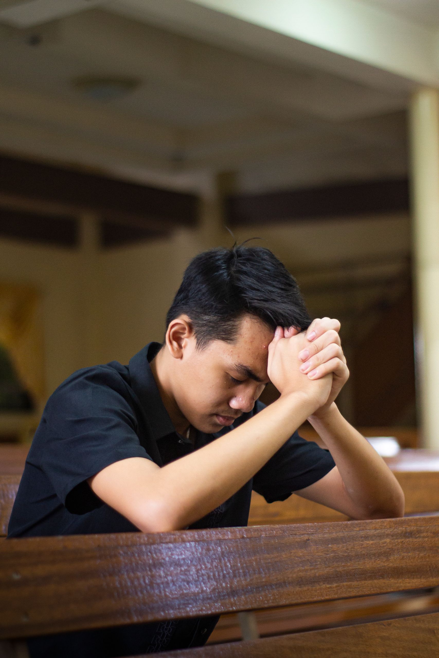 Young adult man in deep prayer with eyes closed inside a church.